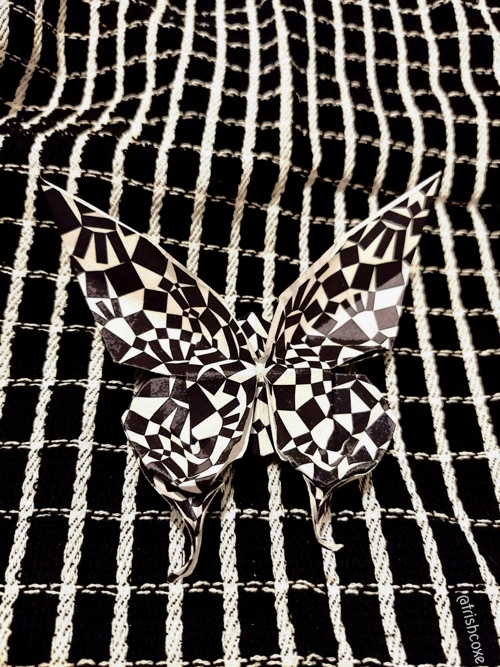 A black and white patterned origami butterfly on top of a blac and white grid background