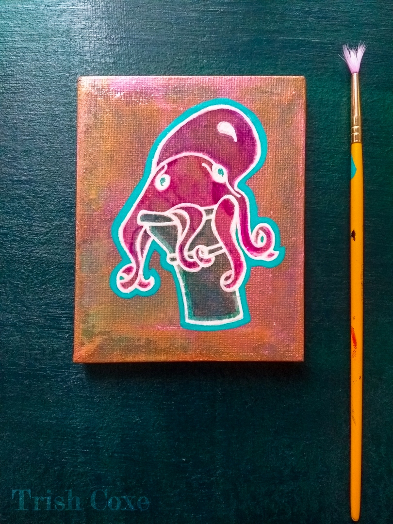 A small canvas, with warm metallic background, painted in a graphic style depicting a magenta octopus seated in a teal ice cream cone. The canvas is shown set beside a small brush to the right on a dark green surface.
